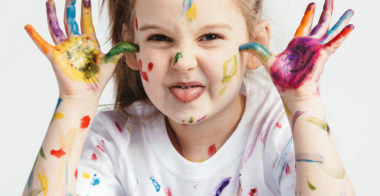 Little girl covered in paint making funny faces. Kindergarten kid. Prankster.